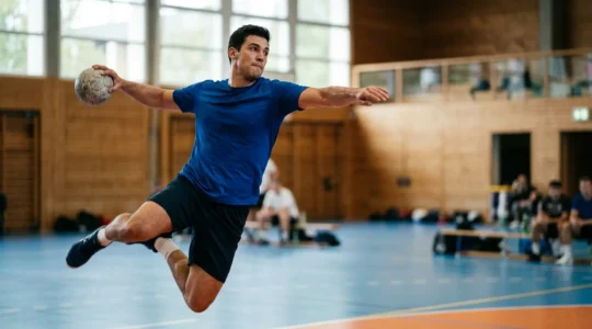 Joueur de handball en pleine action de tir, montrant la puissance musculaire et l'explosivité